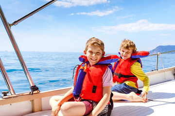 Fototapeta na wymiar Two little kid boys, best friends enjoying sailing boat trip. Family vacations on ocean or sea on sunny day. Children smiling. Brothers, schoolchilden, siblings having fun on yacht.