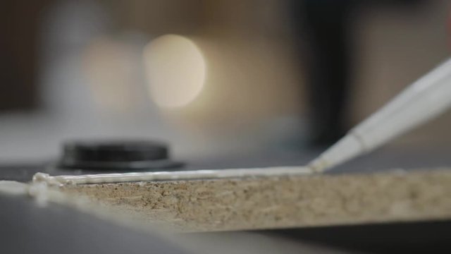 A glue gun put a glue on the black laminated particle board. Hand manufacturing. Craftman works in a workshop.