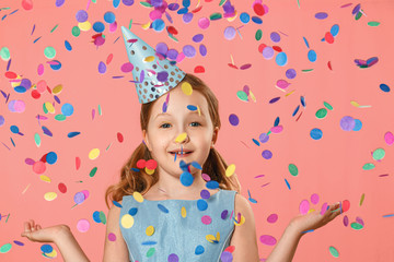 Obraz na płótnie Canvas Cheerful little girl celebrates birthday. A child is standing in a rain of confetti. A party. Closeup portrait on pink background.