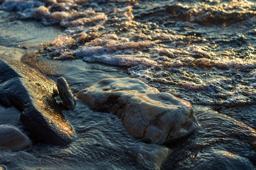 pebble stones on the sea beach, the rolling waves of the sea with foam
