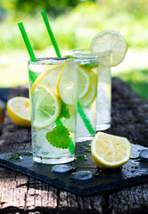 Cold lemonade with lemon slices, mint and ice on a wooden garden table. Cool drinks on a sunny summer day.