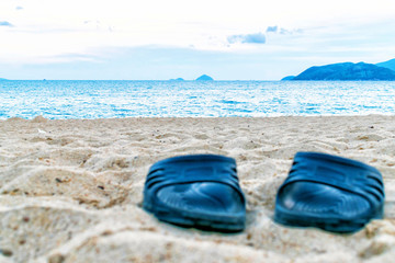 Black slippers on sand on beach with sea on background