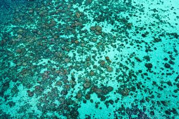Aerial drone top view of the crystal clear lagoon sea water surface with coral reef and sun rays