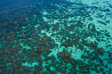 Aerial drone top view of the crystal clear lagoon sea water surface with coral reef and sun rays