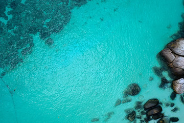 Aerial drone top view of crystal clear lagoon sea water surface with rocks and sun rays