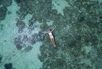 Aerial drone top view of woman floating in crystal clear sea water with coral reef