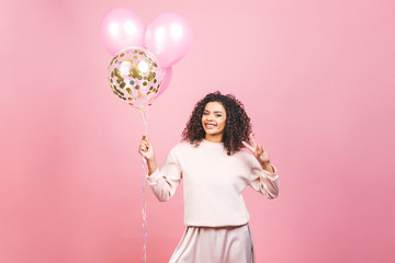 Fototapeta premium Celebration concept - close up portrait of happy cheerful young beautiful african american woman with pink t-shirt with colorful party balloons. Isolated against pink studio Background.