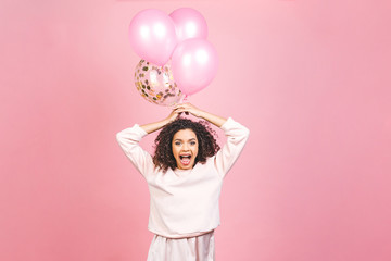 Fototapeta na wymiar Celebration concept - close up portrait of happy cheerful young beautiful african american woman with pink t-shirt with colorful party balloons. Isolated against pink studio Background.