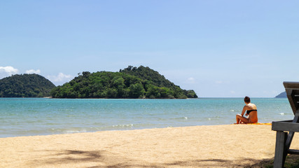 Fototapeta na wymiar Mountain island over the sea with tourist sit down on the beach on the right side with bright sky in background in the afternoon at Koh Mak Island in Trat, Thailand.
