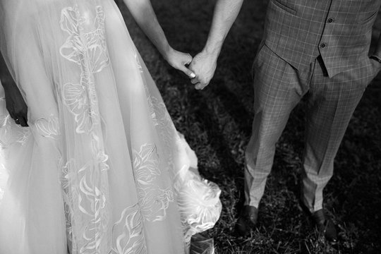 cropped shot of young wedding couple holding hands and walking on grass, black and white image