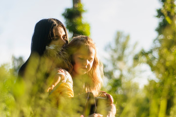 Love between mother and little daughter. Mom and daughter are sitting in the tall grass at sunset - 268851439