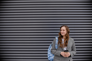 Young woman with beverage laughing near wall