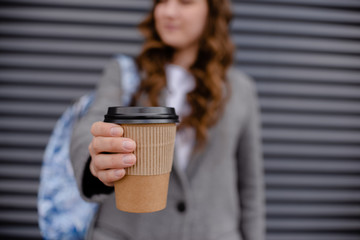 Young woman with beverage laughing near wall