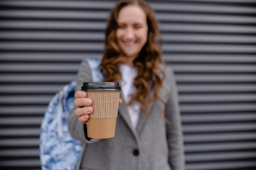Young woman with beverage laughing near wall