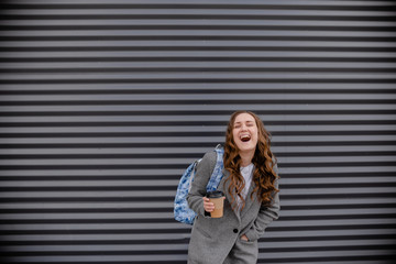 Young woman with beverage laughing near wall