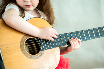 Fototapeta premium Portrait of a little girl with a guitar. For the first time the girl was given a guitar. Nearby sits a teddy bear. A child of 5 years old is studying a musical instrument.