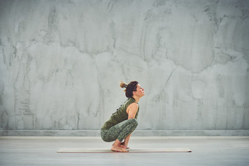 Side view of beautiful Caucasian brunette doing yoga barefoot on mat.