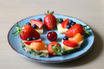 Various spring fruit on a turquoise plate: strawberries, pineapple, blueberries,tabgerine and cherry. Selective focus.