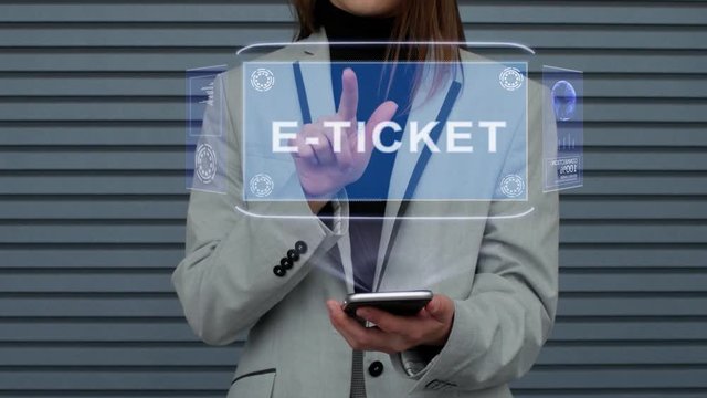 Unrecognizable business woman, interacts with a HUD hologram with text E-ticket. Girl in a business suit uses the technology of the future mobile screen against the background of a striped wall