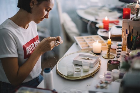 Female creating handmade jewels embroidering with beads and crystals