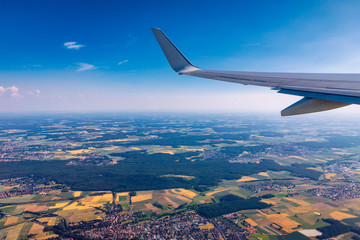 Fototapeta premium Airplane windows view above the earth on landmark down. View from an airplane window over a wing flying high above farmlands and fields. View from window of plane airplane flying.