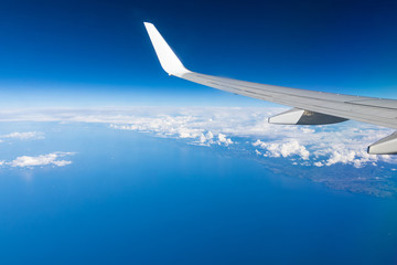 Fototapeta premium View of the wing of an airplane flying above the clouds at high altitude under a blue sky from the passenger window. In flight over Europe. View of jet airplane wing flying in blue sky over clouds.