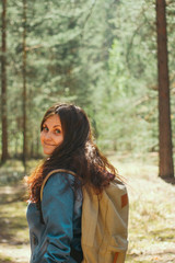 brunette woman with backpack and denim jacket stands  in the woods,selective focus