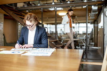 Young business man working on documents at the wooden table in the office or coworking space