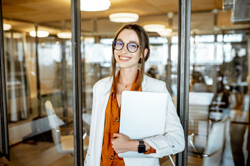 Portrait of a young and cherful business woman standing with laptop in the office