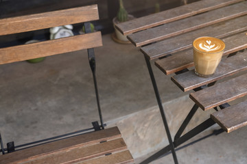 A cup of latte art on wooden table , chair background