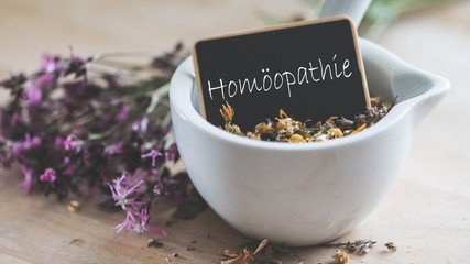 Symbolbild Homöopathie, Mörser mit Schildchen und getrockneten Blüten und Kräutern