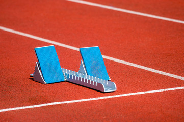 Athletic start block on dark red tartan track