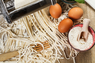 Máquina para hacer pastas caseras espaguettis junto a harina, huevos sobre una mesa de madera. Vista superior y de cerca