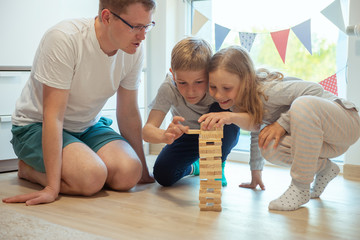 Young happy father playing with his two cute children with wooden blocks