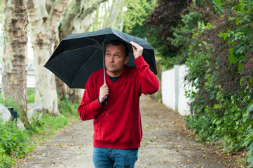 Portrait of man wearing  a red pulllver and blue jeans walking in the street with a black umbrella