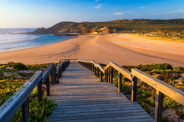 Obraz premium Wooden walkway to the beach Praia da Amoreira, District Aljezur, Algarve Portugal. Panorama from Amoreira beach in the Algarve Portugal. Beach and estuary of the Aljezur river, Praia da Amoreira.