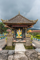Bali, Indonesia - February 25, 2019: Ulun Danu Beratan Temple in Bedoegoel. Colorful Ganesha shrine on entrance checkpoint under dark rainy sky. Green vegetation.
