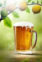 Fresh cold beer on wooden table. Branch of fresh lemons fruits and summer garden background 