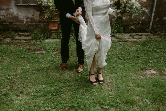 Groom hold train of brides wedding dress on grass