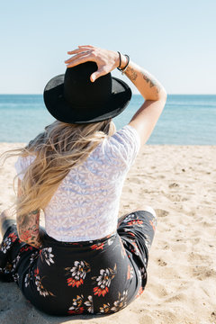 Blonde female sitting on a beach facing the water with her back to camera