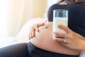 Beautiful pregnant woman holding glass of milk for drinking and touching her belly in morning. Fresh milk is useful, good for fetus or baby and mom. Attractive pregnant woman gets prenatal care