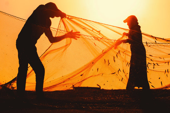 Anonymous, unrecognizable, silhouetted fisherman on the beach shore using fishing net during beautiful, golden sunset