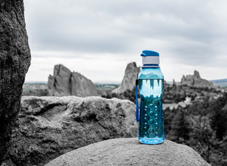 Aqua Blue Fitness Water Bottle Sitting Upon Rock with Mountains in Background. Environmental concept. Fitness concept. Health concept.