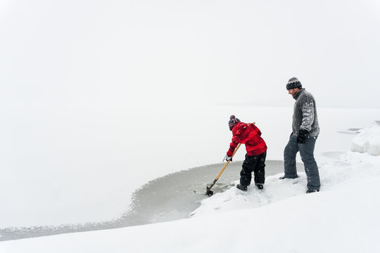 Boy and his father together on snowy adventure using shovel to break the ice