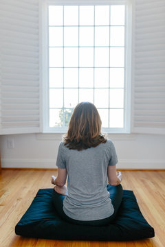 Woman sitting on a meditation cushion facing a big window