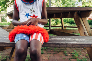 Black girl with USA flag themed outfit sitting on a bench