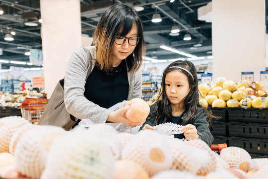 Adorable girl and her Mom choosing fruit in supermarket