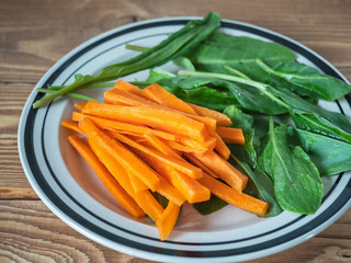 Healthy lunch of chopped carrots and green sorrel on a plate close-up on wooden background