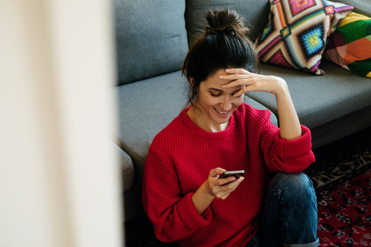 Young woman interact with her smartphone while drink coffee in the living room