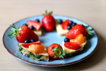 Various spring fruit on a turquoise plate: strawberries, pineapple, blueberries and tangerine. Selective focus.